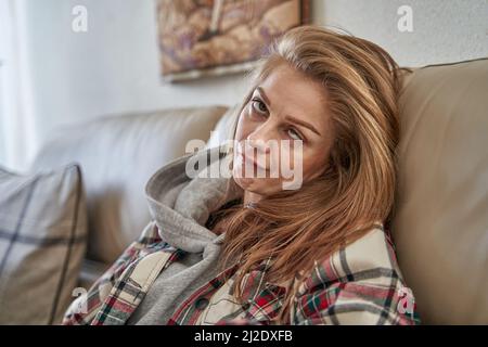 Eine junge kaukasische Frau sitzt auf dem Sofa und grimazing Stockfoto