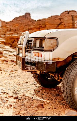 Vorderseite eines 4x4 Autos in der Wüste reg. Linke Seite des vorderen Teils eines vierrädrigen Autos, das im reg mit trockenen Steinen in der Sahara geparkt ist. Stockfoto