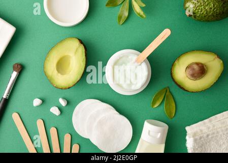 Feuchtigkeitsspendende Creme und Lotion mit Avocado-Extrakt zur Hautpflege mit Toilettenartikeln auf dem grünen Tisch. Draufsicht. Horizontale Zusammensetzung. Stockfoto