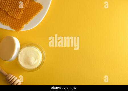 Feuchtigkeitsspendende Hautpflegecreme mit Honigextrakten mit Topf und Teller mit Waben auf gelbem Tisch. Horizontale Zusammensetzung. Draufsicht. Stockfoto