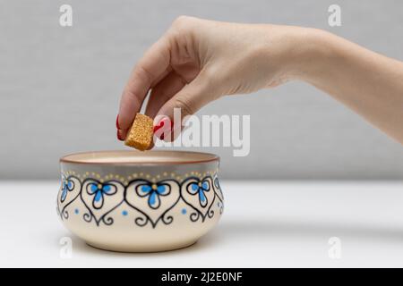 Die Hand einer Frau nimmt einen Würfel braunen Zuckers aus einer Zuckerschüssel. Hochwertige Fotos Stockfoto