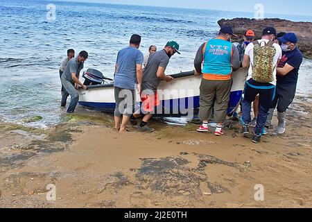 Eine Gruppe, die Fischern dabei hilft, ein Boot aus dem Wasser zu heben. Unterhemd des VTT Clubs. Schiffsname Camilia auf Arabisch. Ain Defla Beach, Gdyel, Cap d’Aiguille. Arzew. Stockfoto