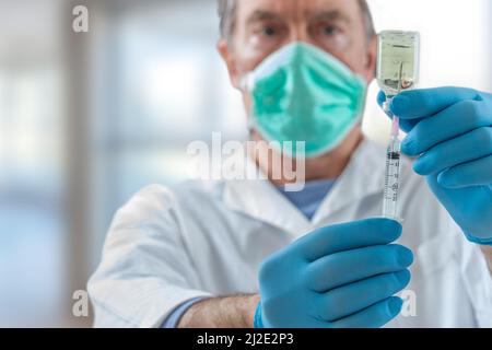 Der Arzt füllt eine Spritze mit Impfstoff auf verschwommenem Hintergrund. Stockfoto