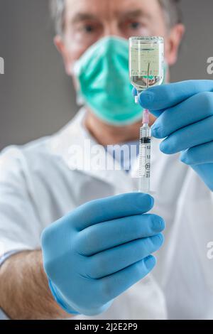 Der Arzt füllt eine Spritze mit Impfstoff auf grauem Hintergrund. Stockfoto