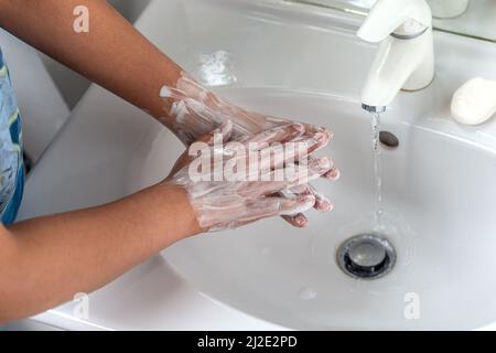 Frau waschen Hand mit Seifenschaum und Leitungswasser im Badezimmer. Hand unter Wasserhahn auf Waschbecken für die persönliche Hygiene zu Grippe und Coronavirus zu verhindern. Gute Verfahren der Handwäsche, um Bakterien, Virus zu töten Stockfoto