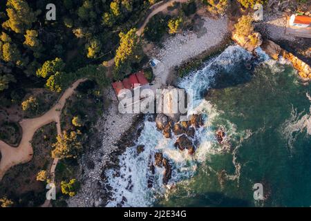 Blick von oben auf eine felsige Bucht neben einem Pinienwald mit einigen Fischerhütten am Kiesstrand, Konzept der Natur und Seefahrt Lebensstil Stockfoto