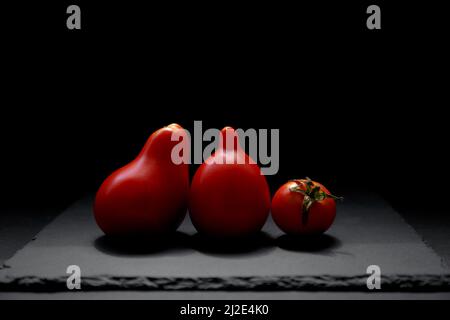 Drei rote Tomaten auf schwarzem Hintergrund. Tomate isoliert, Seitenansicht. Natürliche Antioxidantien in Tomaten Stockfoto