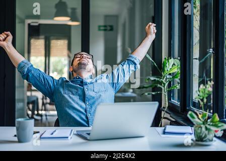 Entspannter erwachsener Mann, der eine kurze Pause von der Arbeit machte, indem er seine Arme streckte. Stockfoto