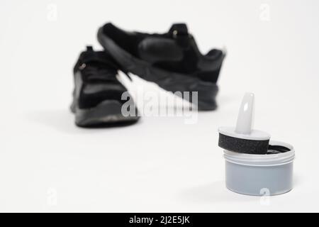 Cremefarbene Farbe für Schuhe und schwarze Kinder-Sneakers auf weißem Hintergrund. Schuhe pflegen. Stockfoto