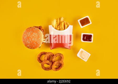 Schnellimbiss von oben. Fleisch Burger, Kartoffelchips und Keile. Nehmen Sie die Komposition mit. Pommes Frites, Hamburger, Mayonnaise und Ketchup-Saucen auf Gelb Stockfoto
