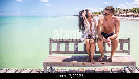 Mann und Frau sitzen und unterhalten sich auf einer Bank neben dem exotischen Meer und genießen ihre Zeit während des Urlaubs im tropischen Paradies. Stockfoto