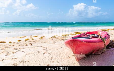 An einem heißen, sonnigen Tag an einem türkisblauen Meer in einem exotischen Reiseziel parkte ein Kajak auf dem rosa Meer an einem Strand. Stockfoto