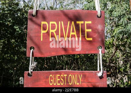 Schild mit der Verschrift „Private and Guests Only“ auf einer gelben Holztafel, die nur Gästen eines tropischen Tourismus-Resorts den Zugang ermöglicht. Stockfoto