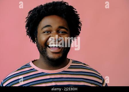 Junger glücklicher afroamerikanischer Mann posiert im Studio über rosa Hintergrund männliches Modell Stockfoto