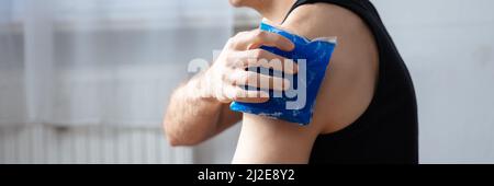 Nahaufnahme der männlichen Trainer Anwendung Cool Gel Pack auf seine verletzte Schulter im Fitnessstudio Stockfoto