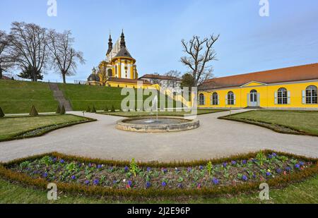 01. April 2022, Brandenburg, Neuzelle: Blick vom Klostergarten auf die katholische Kirche des Klosters Neuzelle. Im Klostergarten Neuzelle in der oder-Spree werden seit rund zwei Jahren die dritte und letzte Bauphase zur Sanierung des Barockgeländes durchgeführt. Hier entstehen eine Baumschule mit Gewächshaus, Küchengarten und Kräutergarten sowie symmetrisch angelegte Blumenbeete, die mit Hecken und Obstbäumen gesäumt sind. Seit 1998 wird an der knapp 5 Hektar großen Gartenanlage gearbeitet, die der einzige Barockgarten Brandenburgs ist. Cr Stockfoto