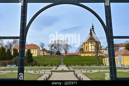 01. April 2022, Brandenburg, Neuzelle: Blick vom Klostergarten auf die katholische Kirche des Klosters Neuzelle. Im Klostergarten Neuzelle in der oder-Spree werden seit rund zwei Jahren die dritte und letzte Bauphase zur Sanierung des Barockgeländes durchgeführt. Hier entstehen eine Baumschule mit Gewächshaus, Küchengarten und Kräutergarten sowie symmetrisch angelegte Blumenbeete, die mit Hecken und Obstbäumen gesäumt sind. Seit 1998 wird an der knapp 5 Hektar großen Gartenanlage gearbeitet, die der einzige Barockgarten Brandenburgs ist. Cr Stockfoto