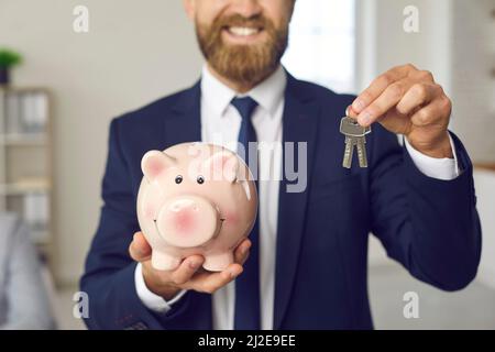 Glücklicher Immobilienmakler oder Hypothekenmakler mit Sparschwein und Schlüssel zum neuen Haus Stockfoto