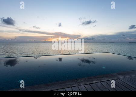 Blick auf einen unendlichen Pool in der Nähe des Ozeans bei Sonnenaufgang Stockfoto