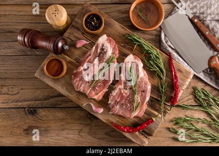 Draufsicht auf einen Holztisch mit gegrillten Schweinesteaks aus Bauernfleisch. Gewürze zum Kochen auf einem Holzbrett Stockfoto