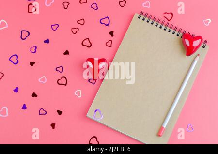Leeres Notizbuch mit Kraftpapier auf einem rosa Hintergrund mit Herzen. Das Konzept des Valentinstag, Muttertag. Nachahmung für Glückwünsche oder Einladung Stockfoto