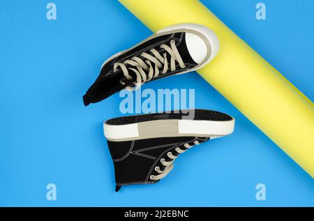 Stylische schwarze Sneaker für Jugendliche auf gelbem und blauem Hintergrund. Sneaker auf farbigem Hintergrund Stockfoto