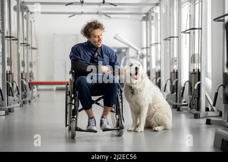 Typ mit Behinderungen im Rollstuhl mit seinem Assistenzhund im Rehabilitationszentrum Stockfoto