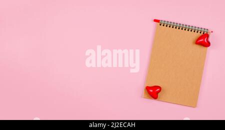 Leeres Notizbuch mit Kraftpapier auf einem rosa Hintergrund mit Herzen. Das Konzept des Valentinstag, Muttertag. Nachahmung für Glückwünsche oder Einladung Stockfoto