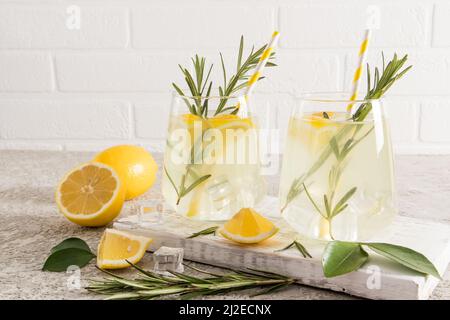 Zwei Gläser köstliche hausgemachte Limonade auf einem Holzbrett gegen eine weiße Ziegelwand und Obst Stockfoto