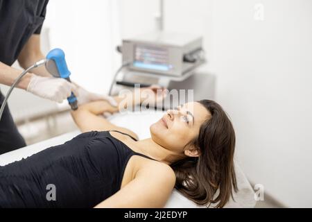 Der Arzt wendet eine Schockwellentherapie auf das Knie der Frau an Stockfoto