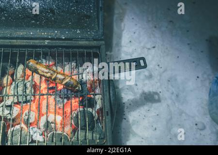 Würstchen auf einem Grill, eine verbrannte Wurst auf einem Holzkohlegrill mit Temperaturmesser im Inneren aufgeklebt. Ablesung von 58 Grad. Stockfoto