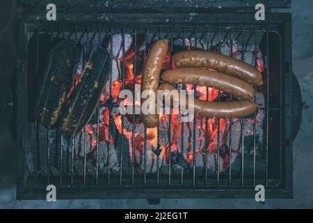 Würste auf einem Grill, mehrere Würste sichtbar und verbranntes Brot auf einem Holzkohlegrill. Blick von oben in der Nacht. Stockfoto