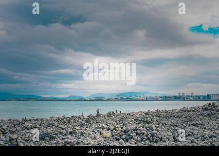 Steinbank vor den docklands oder dem Hafen in Reykjavik, island an einem kalten Sommertag mit Wolken. Reisende Steine oder Haufen sind um gesehen. Stockfoto