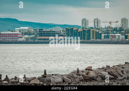 Steinbank vor den docklands oder dem Hafen in Reykjavik, island an einem kalten Sommertag mit Wolken. Reisende Steine oder Haufen sind um gesehen. Stockfoto