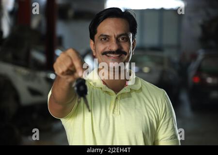 Eine flache Fokusaufnahme eines Indianers in einem Motorladen, der ein gelbes T-Shirt trägt und einen Autoschlüssel hält Stockfoto