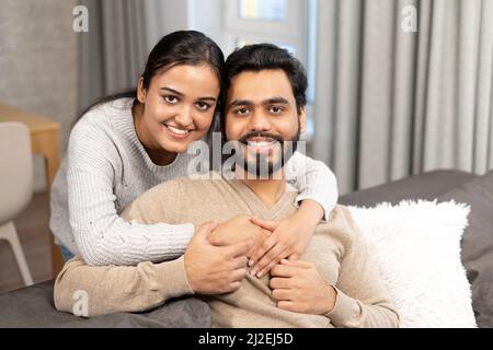 Sanftes und liebes verliebter Paare, die auf dem bequemen Sofa zu Hause umarmt sitzen und die Kamera betrachten. Konzept der Unterstützung und Fürsorge in der Ehe Stockfoto