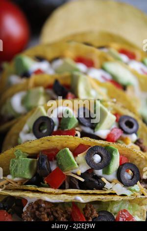 Tacos aus Maistortillas, Hackfleisch, geschreddertem Cheddar-Käse, schwarzen Oliven, Avocados, Salat, saure Rahm und Tomaten. Selektiver Fokus mit blu Stockfoto