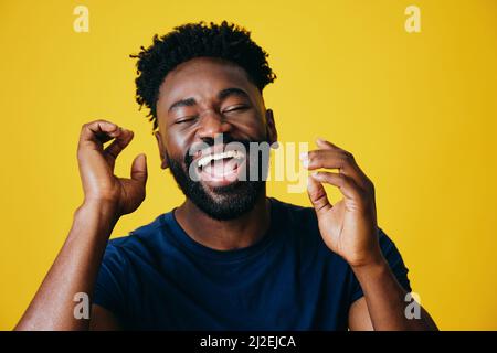 Porträt eines verspielten Afro-Mannes mit geöffneten Händen vor gelbem Hintergrund Stockfoto