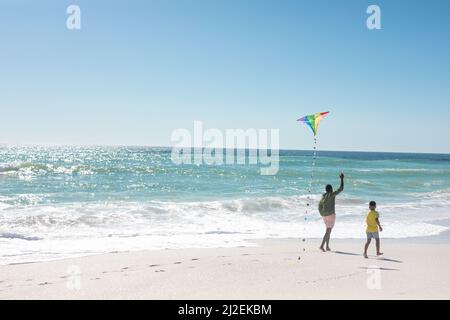 afroamerikanischer Vater und Sohn laufen am sonnigen Tag mit Drachen am Strand mit Kopieplatz Stockfoto