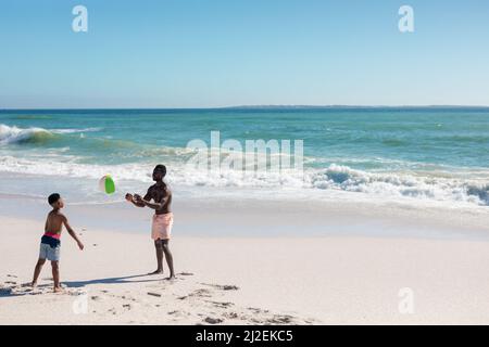 Die ganze Länge der afroamerikanischen Vater und Sohn spielen mit Ball am Strand an sonnigen Tag Stockfoto