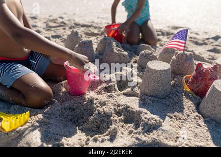 Midsection von afroamerikanischen Bruder und Schwester, die gemeinsam am Strand am sonnigen Tag Sandburg bauen Stockfoto