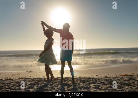 Ein glückliches afroamerikanisches Paar, das am Strand gegen den Himmel tanzt Stockfoto