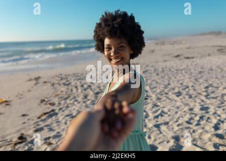 Glückliche afroamerikanische Frau, die am sonnigen Tag am Strand eine kurze Hand des Freundes hält Stockfoto