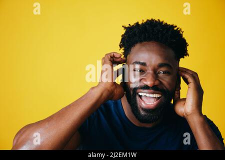 Porträt eines verspielten Afro-Mannes mit offenem Mund, der die Ohren vor gelbem Hintergrund berührt Stockfoto