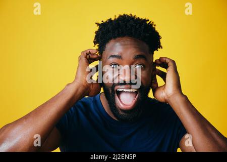 Porträt eines verspielten Afro-Mannes mit offenem Mund, der die Ohren vor gelbem Hintergrund berührt Stockfoto