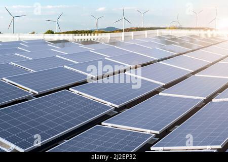 Installierte Sonnenkollektoren im Vordergrund und Windturbinen im Hintergrund. Konzept der grünen sauberen und erneuerbaren Energie. Stockfoto