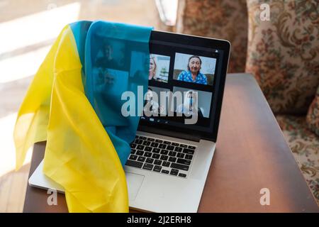 Flagge der Ukraine auf dem Hintergrund und breiten digitalen Bildschirm des Laptops mit Videokonferenz. Krieg mit Russland. Cyberangriff, Sanktionen, wirtschaftlicher Zusammenbruch Stockfoto