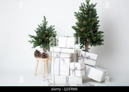 Moderne Weihnachtsdekoration auf weißem Hintergrund mit weiß gewickelten Weihnachtsgeschenken und silbernem Band, zwei Miniatur-Weihnachtsbäumen Stockfoto