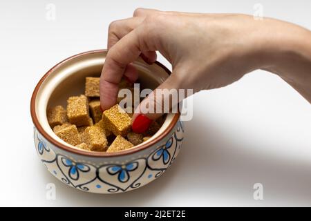 Die Hand einer Frau nimmt einen braunen Zuckerwürfel aus einer Zuckerschüssel. Hochwertige Fotos Stockfoto