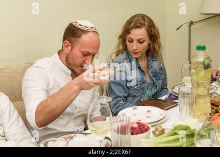 Jüdische Familie feiert Passah Seder. Der junge Mann liest die Passahhaggada, hebt ein Weinglas. Jüdische Familie am Tisch mit traditionellem Essen, das Pesach feiert. Stockfoto